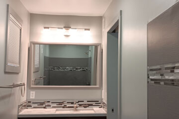 bathroom addition remodel with pocket door and tile walls and mosaic tile with large mirror and vanity